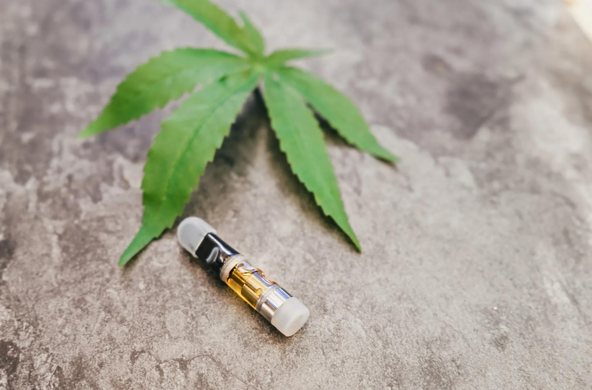 Cannabis leaf and vape cartridge on concrete surface